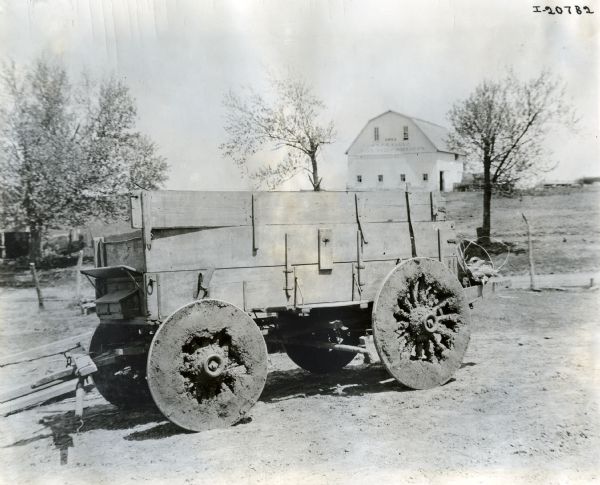 A wagon with mud-caked wheels sits loaded with bushels of corn. There is a large barn in the background. The text on the barn reads: "1912; W.S. Bealuce; Live Stock Breeders."