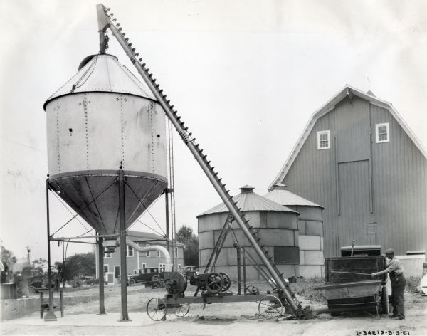 A farmer fills what appears to be a large water tank on a farm using a stationary engine.