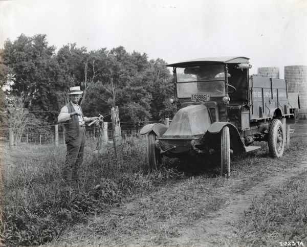 International model "F" or "31" truck operated by Geo. E. Morse Farms of Ladora.  A man stands behind a barbed wire fence with tools in his hand near the truck.