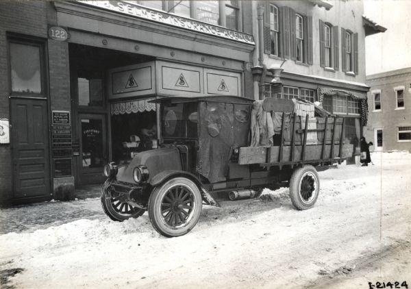 International model "F" or "31" truck. The truck was photographed on a snowy street in front of a building housing the Selmer Insurance Agency, New England Mutual Life, and the Chippewa Valley Transfer Co.