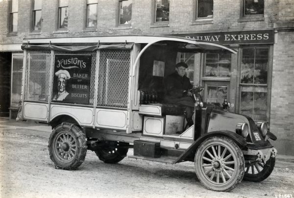 International model "F" or "31" truck operated by Huston's "Baker of Better Biscuits." A man is sitting in the driver's seat of the truck, and there are chains on the truck's rear tires.