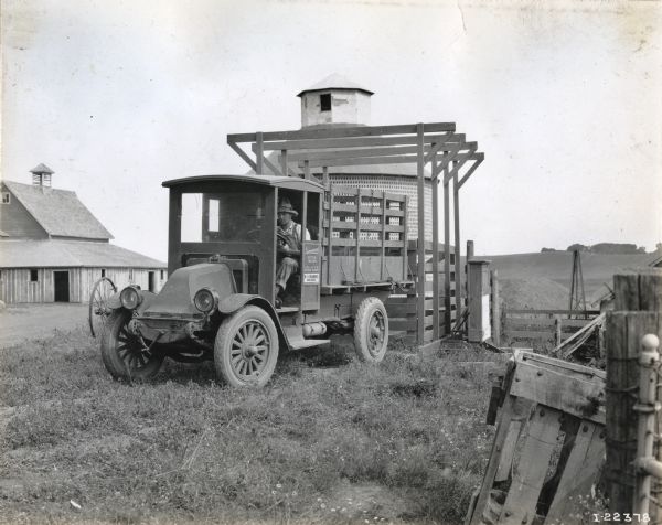 International model "F" or "31" truck operated by W.H. Brammer of Coon Rapids. The truck is parked in front of several buildings, with a man in the driver's seat. There is a large silo behind the truck.