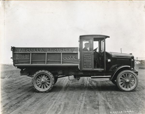 International Model 63 truck operated by Arquilla Borthers. The truck was photographed with a man in the driver's seat. Printing on the side of the truck reads: "Building Material" "Coal". "Call Chesterfield, O111" "Yards 93rd St. and I.C. Tracks Office 9348 Cottage Grove Ave."