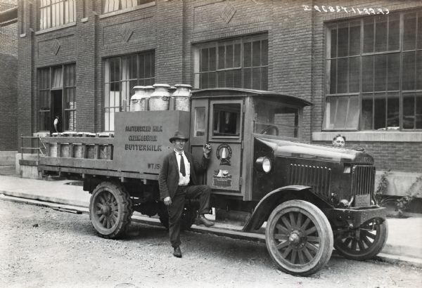 International Model 63 truck operated by York Sanitary Milk Co. There are two men standing outside of the truck. The truck was photographed outside the company's building and is carrying milk containers. The side of the truck advertises "Pasteurized Milk, Cream & Butter, Buttermilk, and Purity Ice Cream."