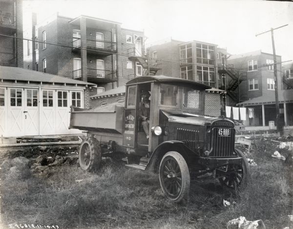 International Model 63 truck operated by C.M. Berry, "contractor" of Webster Groves. The truck was photographed with a man in the passenger seat in the backyard of apartment buildings. The truck is filled with dirt, sand or gravel(?).
