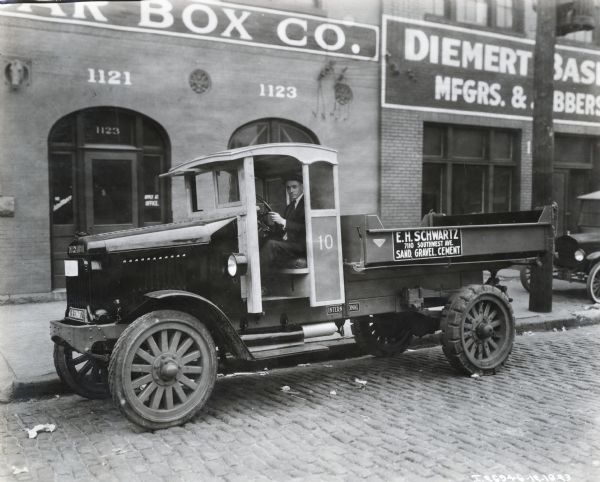 International Model 63 truck operated by E.H. Schwartz. The truck was photographed on a city street with a male driver. The address is printed on the side of the truck along with the words "Sand, Gravel, Cement." Possibly photographed in St. Louis, Missouri.