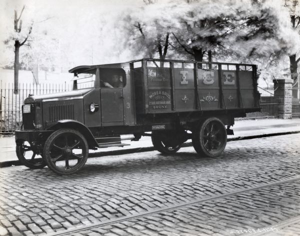 International Model "63" truck operated by Morea Bros. of Bronx, New York. There is a man in the driver's seat, and the truck is on a cobblestone street with cable car tracks running down the middle. The side of the truck advertises ice and provides the phone number "Tel. Fordham 9710" and the address "2388 Arthur Ave." A small plaque on the side of the truck reads: "New York City Ice Dealer 1924  Truck No. 5467 Department of Public Markets".