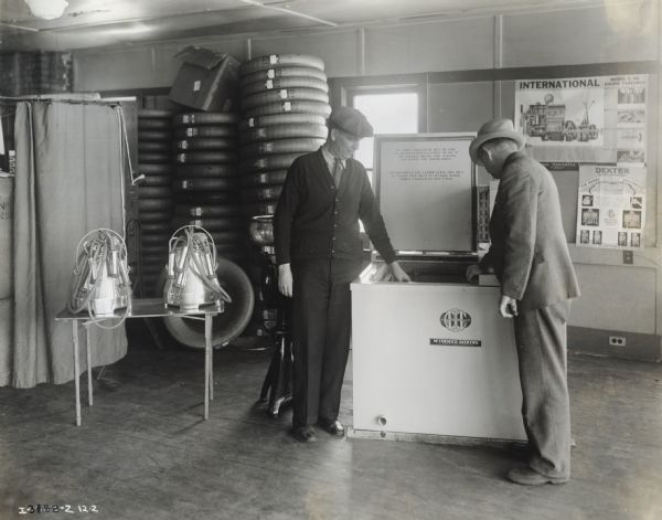 Day and Perkins, McCormick-Deering dealers, stand by a milk cooler and milking machines in their dealership showroom.