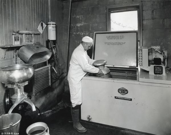 Clifford C. Ball places a milk can into a McCormick-Deering 6-can milk cooler. A cream separator stands against the wall to the left.