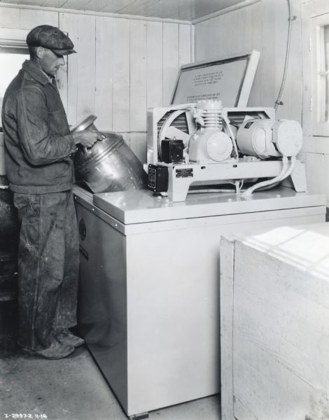 A man places a milk can into a McCormick-Deering 6-can milk cooler on the farm of Mrs. Joe Schmidt.