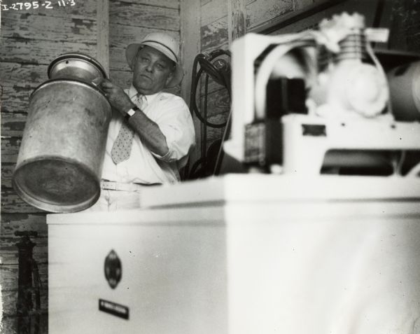 A man lifts a milk can into an International Harvester milk cooler.