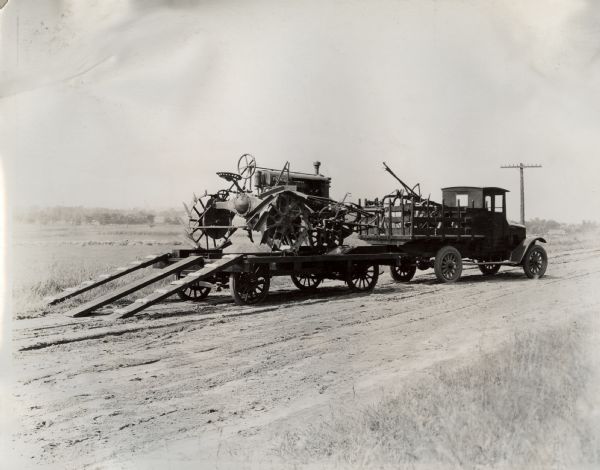 A Farmall Regular tractor is loaded onto a trailer pulled by an International Model S truck before or after a demonstration.