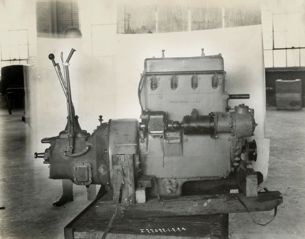 Engine for an International truck, most likely a model 63.  This side view of the engine was photographed on a wooden table or sled? A man can be seen behind the engine supporting a white backdrop.