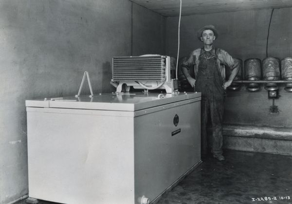 Milton Stump stands with his hands on his hips next to a McCormick-Deering 8-can Milk Cooler. Multiple upside-down milk canisters are on the wall behind Mr. Stump.