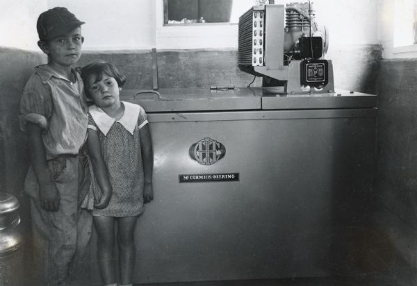 Two children, Charles and Lois, stand next to a McCormick-Deering 6-can milk cooler. The children are the grandchildren of Paul Myers.