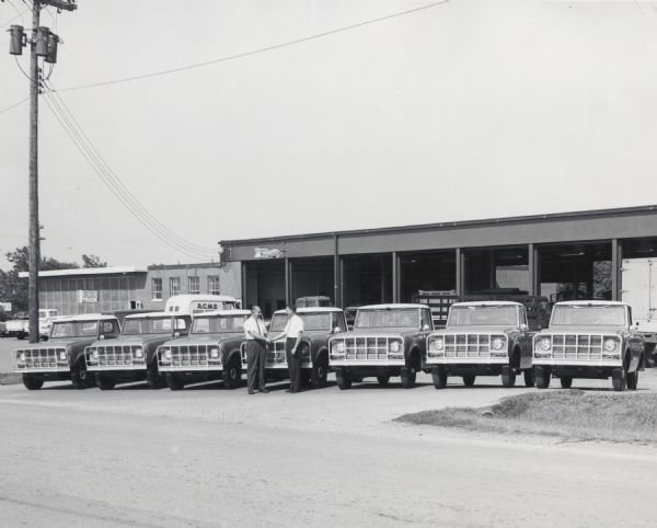 Two men shaking hands in front of a fleet of seven Scout 80 (4x4) Cab-Tops, presumably just purchased by the Tennessee Game and Fish Commission. As an "International Truck" banner can be seen on one of the buildings in the background, the photograph was probably taken at an International Truck dealership.