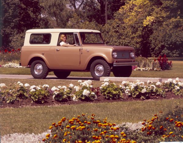 A woman sits in the passenger seat of a International Harvester Scout 80 4x4 travel top vehicle parked in a floral setting.