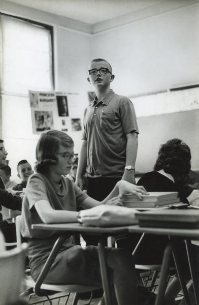 Thirteen-year-old student John "Butch" Quirk stands in a classroom surrounded by his seated classmates. The original magazine caption reads: "School Boy: 'Butch' Quirk is a bright seventh grader, typical except for size-5 feet 8 inches, 175 pounds."