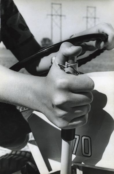 Thirteen-year-old John "Butch" Quick is photographed driving a Cub Cadet tractor. This close-up captures one of Butch's hands on the steering wheel and the other on the stick shift.