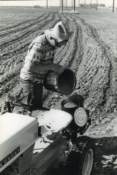Thirteen-year-old John "Butch" Quick is photographed filling the hopper of his Cub Cadet tractor with fertilizer.