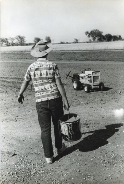Thirteen-year-old John "Butch" Quick carrying a bucket of seed toward his Cub Cadet tractor.