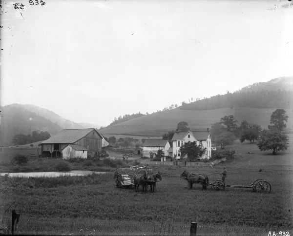 Scenic view of rural farmstead with horse-drawn McCormick grain binder and wagon in field in front of farmhouse.