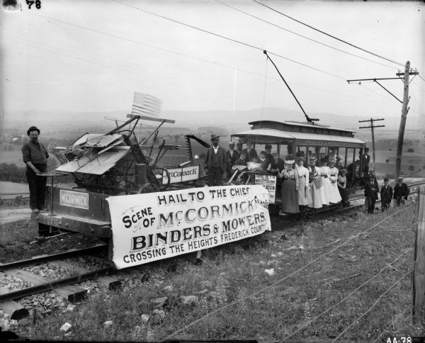 Group of people posing on a trolley car, which is pulling a flat car loaded with a McCormick grain binder and mower as part of an event culminating the "Crossing the Heights, Frederick County," Virginia, as indicated on the banner. Trolley car owned and operated by Frederick and Middleton Railway. On the side of the flat car is a banner that reads: "Hail to the Chief, Scene of McCormick, Binders and Mowers crossing the heights of Frederick County." The sign on the side of the railroad car reads: "Frederick & Middletown Railway." Another sign at the front of the car is for the "Knights of Pithias Picnic."