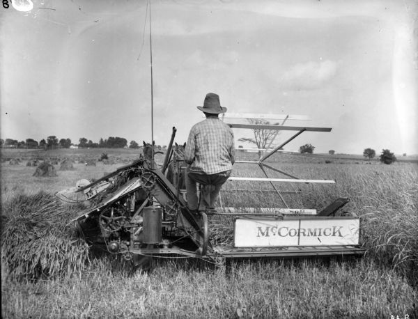 Rear view of a McCormick horse-drawn grain binder operated by a farmer in a field.