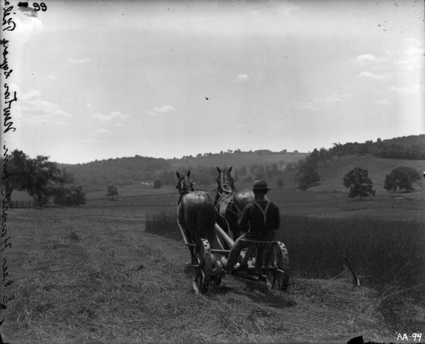 Rear view of a farmer operating a horse-drawn mower in a field. The words "E Rees Howard Farm. Newton Square Phila." have been etched into the emulsion of the negative along the left vertical side of the image.