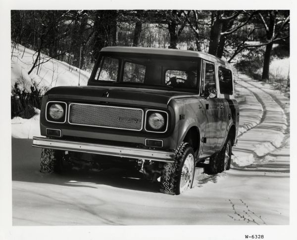 A man leaves tracks in the snow as he drives an International Harvester Scout truck through a wooded area.
