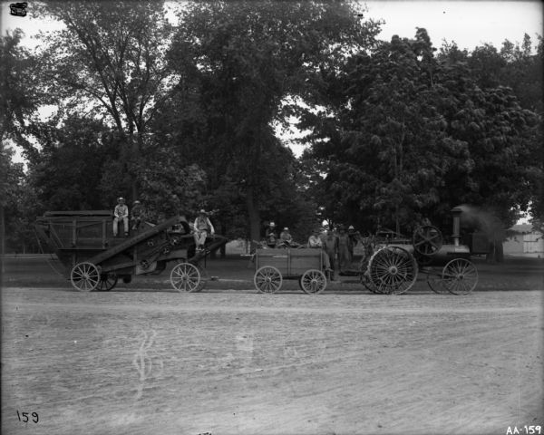 A group of men are posing on and around a steam tractor hooked up to a wagon and a New Peerless thresher.