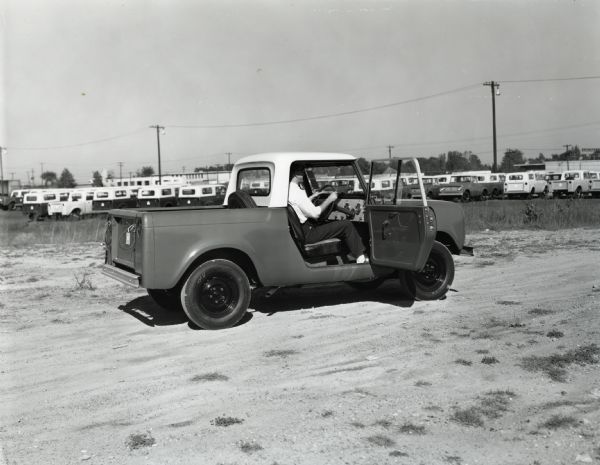 Rear and side view of a man sitting in the driver's seat of a right-hand drive Scout. The driver-side door is open to allow a view of the steering wheel and dash.