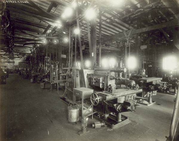 The factory floor with equipment used to build parts and materials. The stations have motors attached to belts, which are attached to the ceiling with pulleys. The factory manufactures 4 cylinder engines for general and farm work.