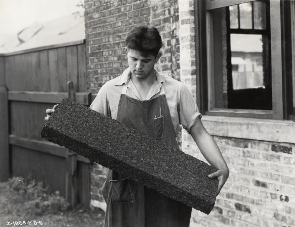 A factory worker at the West Pullman Works holds a block of cork insulation for a McCormick-Deering Milk Cooler.