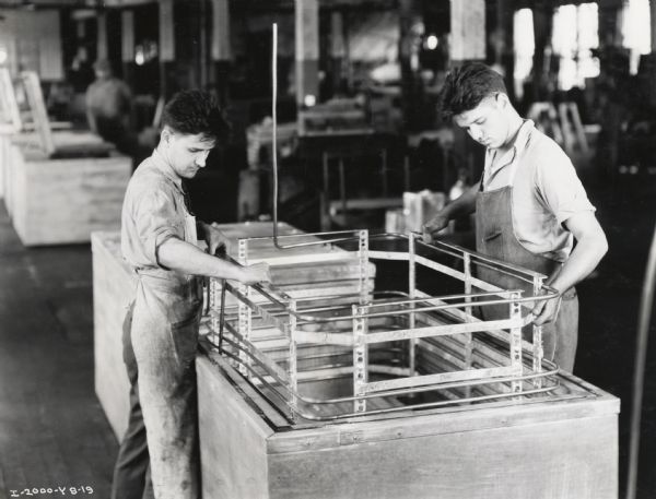 Factory workers at International Harvester's West Pullman Works assemble a McCormick-Deering 6-can milk cooler. The men are placing cooling coils and the coil frame into the milk cooler.