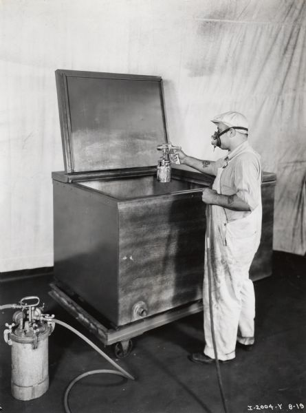 A factory worker at International Harvester's West Pullman Works spray paints the interior of a 6-can McCormick-Deering milk cooler.