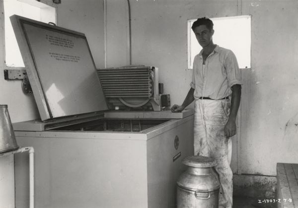 A man (identified as Earl Atkinson) stands next to a McCormick-Deering Milk Cooler.  A milk container sits at his feet.