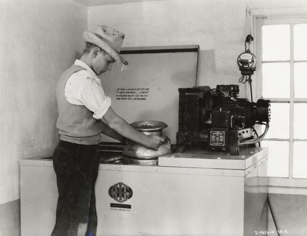 A man places a milk canister into a McCormick-Deering milk cooler. 
