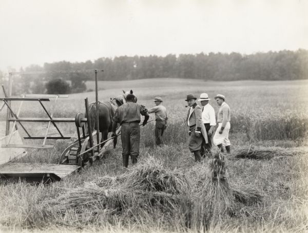 A production still from the Fox Hearst film "Romance of the Reaper". The film was produced by International Harvester at Walnut Grove to celebrate the Reaper Centennial. Caption on back of photograph reads: "Trying out the 1831 reaper. Jo Anderson (played by Harry Wilson); Frank Carson, general utility man; A.C. Seyfarth wearing Cyrus Hall McCormick's dress coat; H.A. Kellar and Edgar L. Kaw."