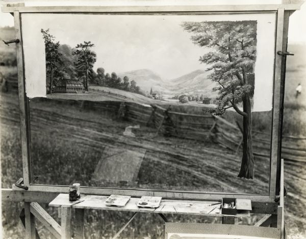A backdrop from the set of the Fox Hearst film "Romance of the Reaper." The film was produced by International Harvester at Walnut Grove to celebrate the Reaper Centennial. Caption on back of photograph reads: "Painting on glass approximately 4 x 6 feet. Mounted in frame on scaffold carrying on upper portion painting of simulated background for main public reaper trial scene. Also, painting of tree for foreground of same scene. Blurred fence below is actual fence but is out of focus."