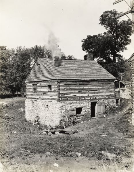A production still for the Fox Hearst film "Romance of the Reaper". The film was produced by International Harvester at Walnut Grove to celebrate the Reaper Centennial. Caption on back of photograph reads: "Forge shop. Reaper in early stage of development shown in foreground. Smoke shown was testing of chimney with smudge pots."