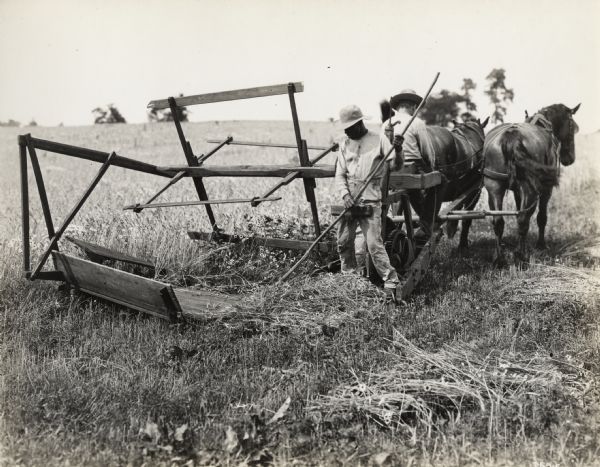 A production still for the Fox Hearst film "Romance of a Reaper". The film was produced by International Harvester at Walnut Grove to celebrate the Reaper Centennial. Two men, one driving a team of two horses and another raking grain, operate a replica of the 1831 reaper.
