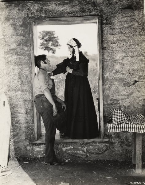 A production still for the Fox Hearst film "Romance of the Reaper". The film was produced by International Harvester at Walnut Grove to celebrate the Reaper Centennial. Del McDermid (in the role of Cyrus McCormick) and Miss Geraldine Woods (as Miss Mary Ann McCormick) stand in the doorway of a farm building.