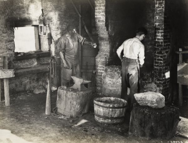 A production still for the Fox Hearst film "Romance of the Reaper". The film was produced by International Harvester at Walnut Grove to celebrate the Reaper Centennial. Harry Wilson (playing the role of Jo Anderson) and Del McDermid (playing the role of Cyrus Hall McCormick) work in the forge shop.