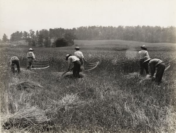 Men cutting grain with cradles while other men gather it into bundles by hand. The scene is a re-enactment filmed in 1929 for the Fox-Hearst film "Romance of the Reaper." The film was produced by International Harvester to celebrate the Reaper Centennial.