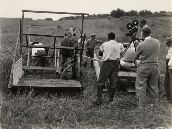 A production still for the Fox Hearst film "Romance of the Reaper." The film was produced by International Harvester at Walnut Grove to celebrate the Reaper Centennial. Actors and crew members with a camera are gathered around a replica of McCormick's first reaper.