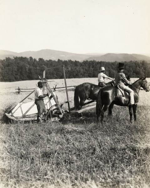 A production still for the Fox Hearst film "Romance of the Reaper". The film was produced by International Harvester at Walnut Grove to celebrate the Reaper Centennial. Two men ride horses in front of a replica of McCormick's first reaper. The man wearing the top hat is actor Del McDermid (in the role of Cyrus Hall McCormick). The man walking behind the horses alongside the reaper is Harry Wilson, who played the role of Jo Anderson in the film.