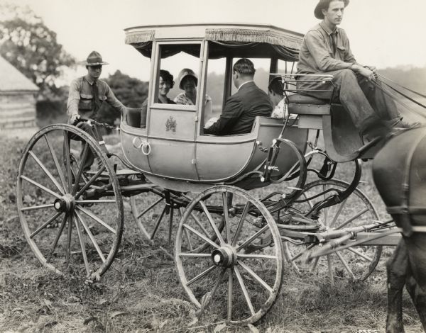 A production still for the Fox Hearst film "Romance of a Reaper." The film was produced by International Harvester at Walnut Grove to celebrate the Reaper Centennial. There is a male driver, three women and a man sitting in the carriage, and another man climbing into the carriage from the back.