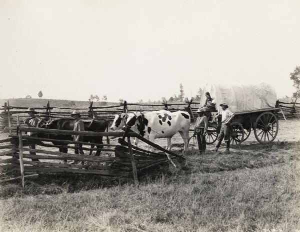 A production still for the Fox Hearst film "Romance of the Reaper." The film was produced by International Harvester at Walnut Grove to celebrate the Reaper Centennial. Four men stand near a covered wagon and its team while a woman with a young infant sits in the wagon.