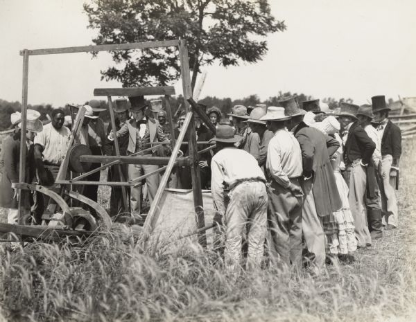 A production still for the Fox Hearst film "Romance of the Reaper." The film was produced by International Harvester at Walnut Grove to celebrate the Reaper Centennial. In this scene Cyrus McCormick (as played by actor Del McDermid) describes the features of his reaper to a crowd of onlookers. The machine is a replica of the first McCormick reaper.